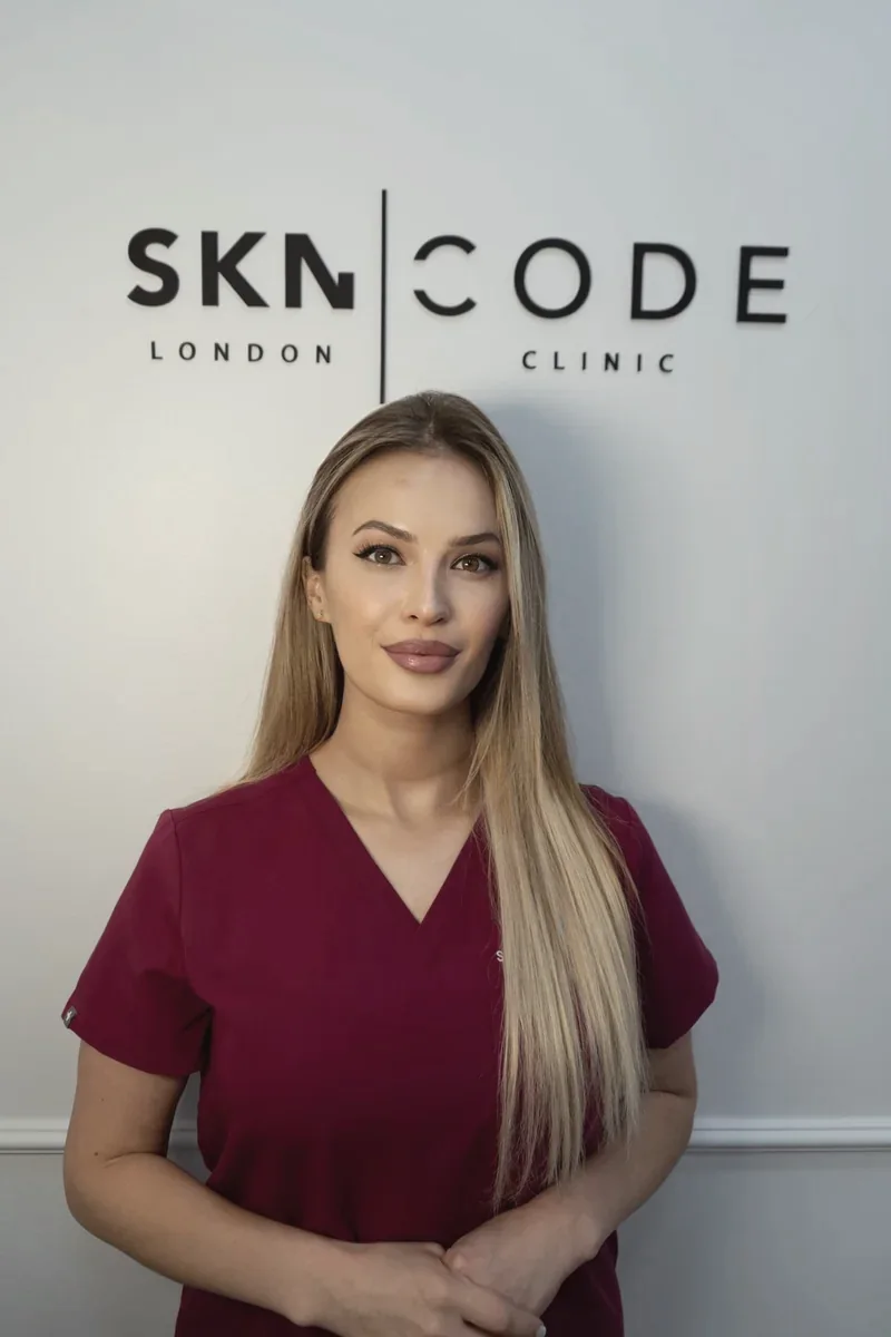 Alkelida, aesthetic practitioner, in burgundy scrubs in front of the SKNCode London Clinic sign
