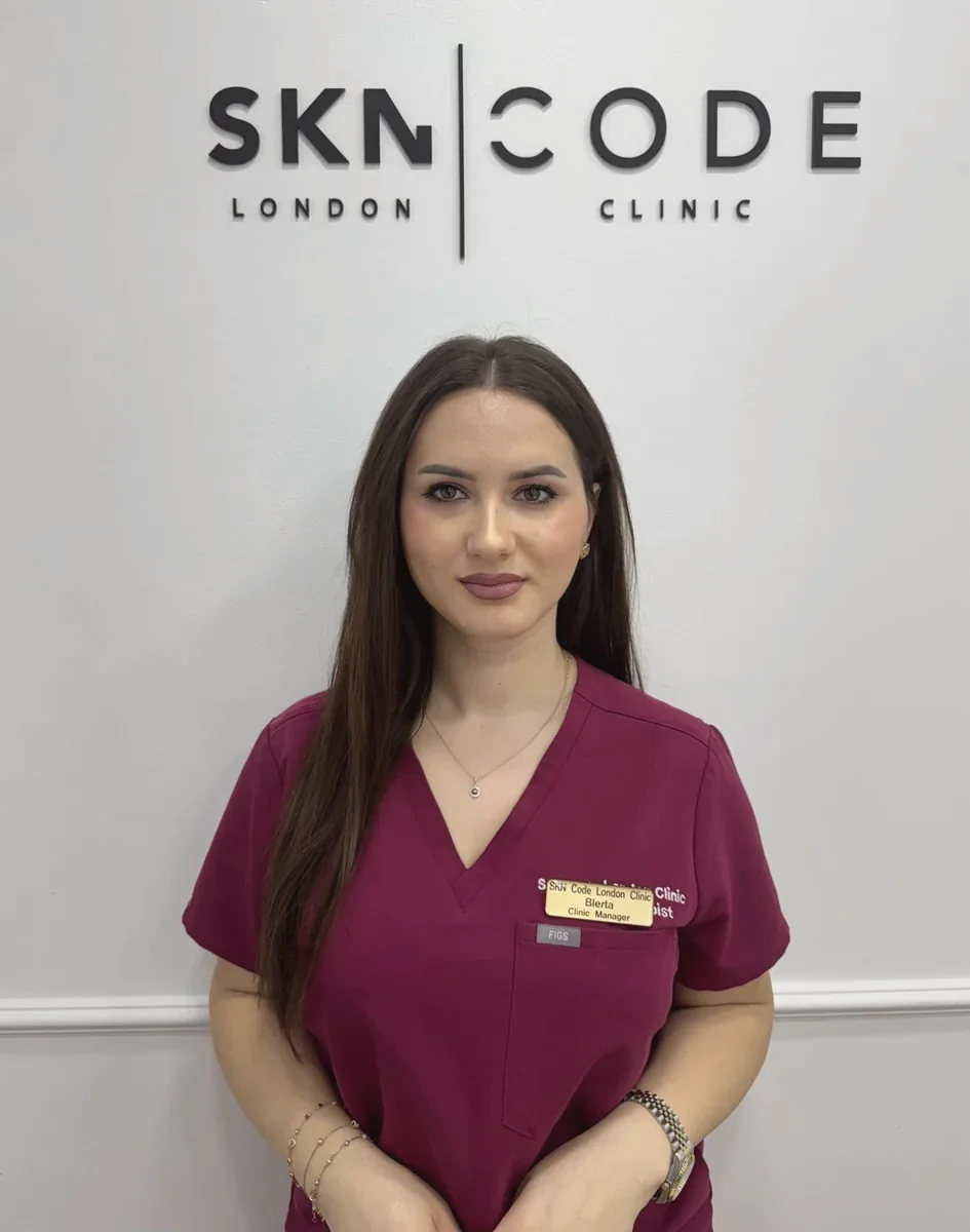 Blerta, Clinic Manager, in burgundy scrubs in front of the SKNCode London Clinic sign